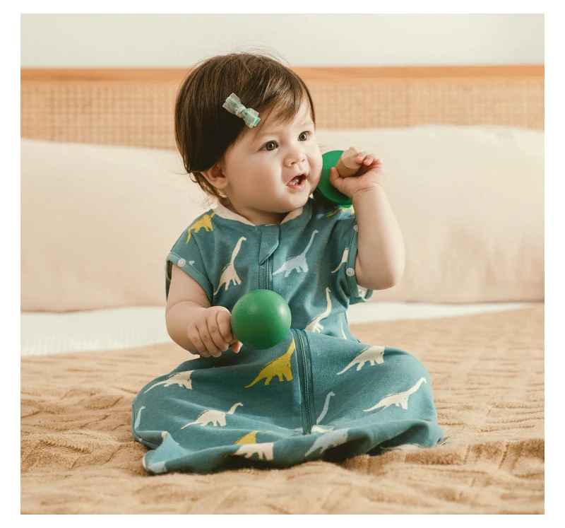 enfant assis sur le lit des parents dans sa gigoteuse dinosaure entrain de jouet avec des maracas