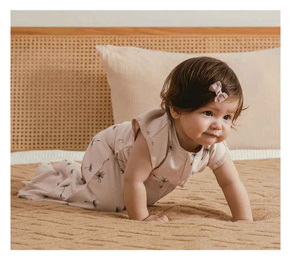 petite fille qui est a quatre pattes sur le lit avec sa gigoteuse écru avec des fleurs de pissenlits