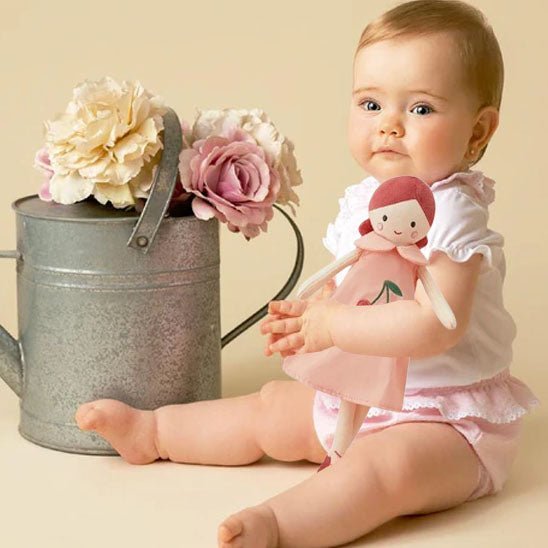 petite fille qui tiens la poupée dans les mains avec un arrosoir rempli de fleurs devant elle